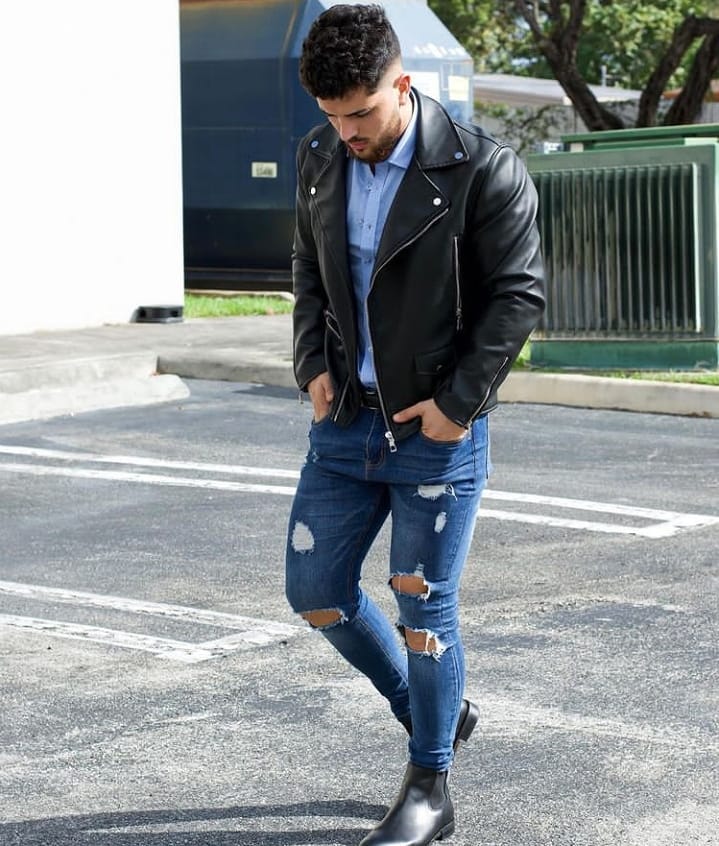 Man wearing a leather jacket over a dress shirt with ripped jeans